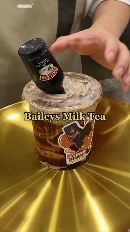 A cup of brown sugar milk tea with a mini bottle of Baileys tipped upside down into the lid