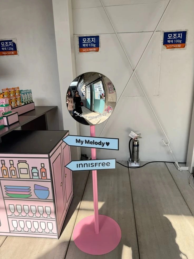 A round mirror on a pink pole, with two arrow-shaped signs pointing the way