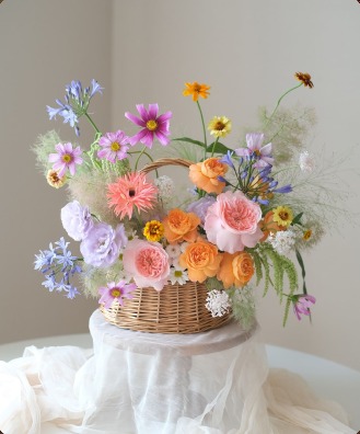 Wicker basket of garden roses, cosmos and wildflowers on draped linen