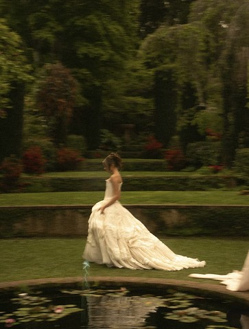 Bride walking across a garden lawn by a lily pond