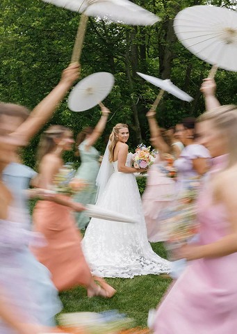 Bridesmaids in pastel dresses twirling parasols around the bride