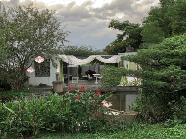 The pond-side arbor at dusk with lush greenery and glowing lanterns